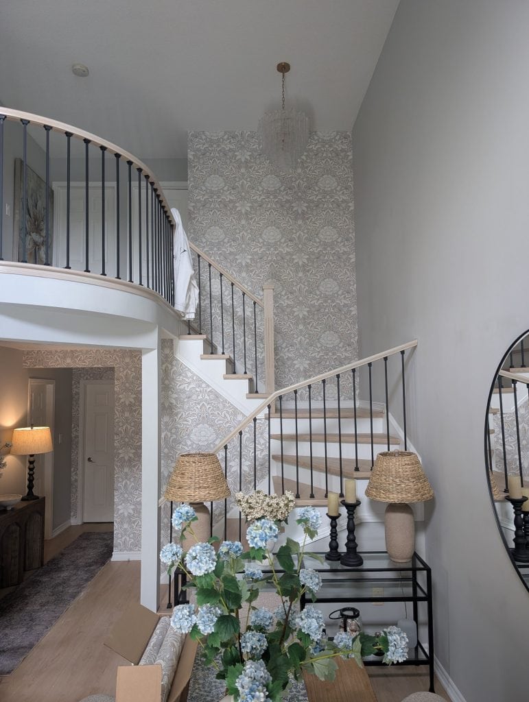 Elegant stairway wallpaper installation in a Hamilton home featuring a soft neutral botanical pattern, curved staircase, high ceilings, and bright contemporary finishes. Professional wallpaper installation by DW Painting & Wallpapering.